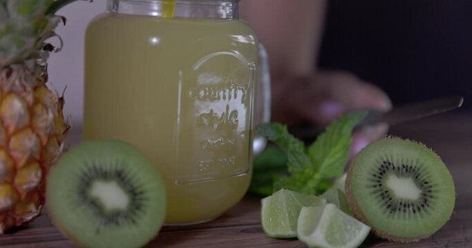 Natural juice mug with pineapple, kiwi and lime. With blurred woman's body in background.