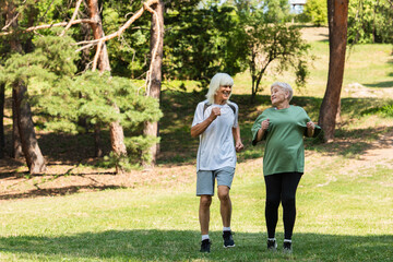 full length of senior couple in sportswear running in green park.