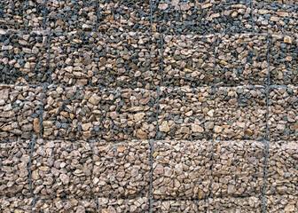 Gabion with heaps of small stones in a grid as the city or garden decoration, textured background