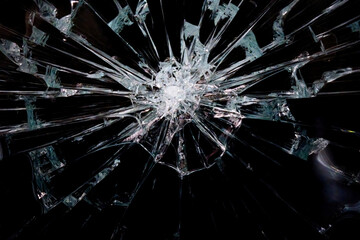 A broken glass surface, with a wide center and many sharp shards originating from it. Black...