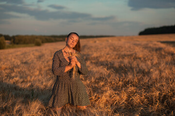 A girl with a bouquet of wheat ears stands in a wheat field at sunset