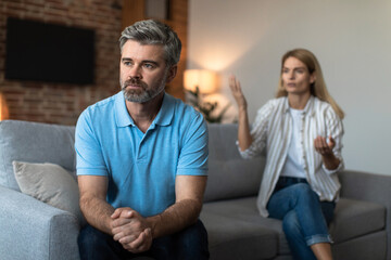 Offended unhappy mature caucasian woman scolds at sad husband, man ignores wife in living room interior