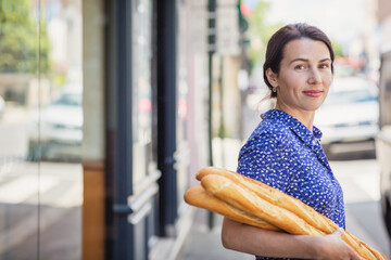 Young pretty woman buying a french baguette and standing on the street in city