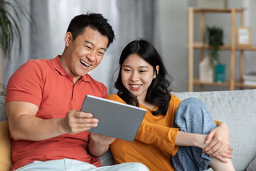 Cheerful asian family sitting on couch at home, using pad