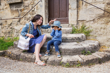 Mother and little handsome baby boy sitting on ancient stone stairs and playing outdoor with straw hat in old town