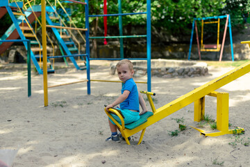 Fototapeta na wymiar Lonely little boy is playing on the playground. The boy is sitting on a swing all alone