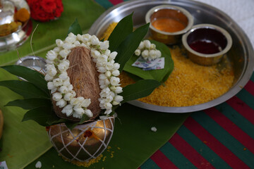 closeup view of coconut decorated with jasmine flower on a brass vessel  with yellow rice, petal leaf. sandal and kumkumam put on a plate during a religious function