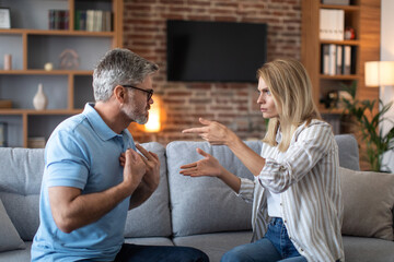 Upset offended angry excited mature caucasian husband and wife quarreling in living room interior,...