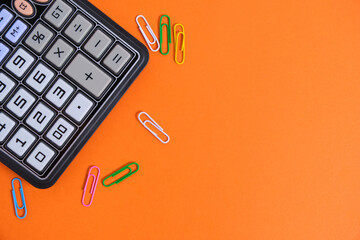 Calculator and colorful paper clips on an orange background.School supplies.