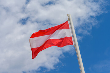 Austrian flag waving in the wind. It is a beautiful sunny summer day, with blue sky and white clouds in the background.