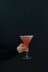 Woman's hand holding red cocktail with Halloween decoration on black background. Copy space.