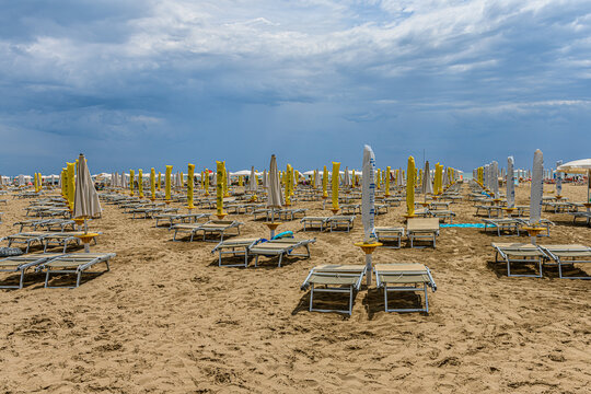 Beach in Caorle, Italy, with rows of sun beds and closed parasols. The beach is almost empty, except for a few people close to the sea. Empty beds and closed parasols could symbolize the end of season