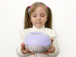 A little funny girl with ponytails inhales essential oils from a diffuser from a humidifier. Device...