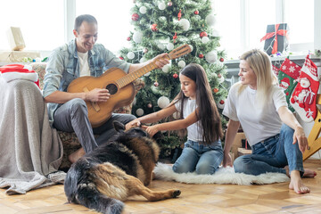 Excited girl and her family sitting on the floor near christmas tree and smiling. family during Christmastime