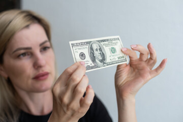 Woman holding dollar bill and looking at it with watermarks closeup. Counterfeiting money concept.