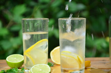 Fresh summer drink. Cold lemonade with mint lemon and lime on a nature outdoor background. Mojito summer refreshing cocktail with ice and mint
