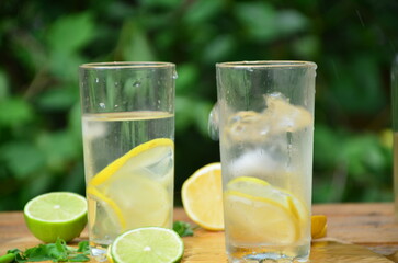 Fresh summer drink. Cold lemonade with mint lemon and lime on a nature outdoor background. Mojito summer refreshing cocktail with ice and mint
