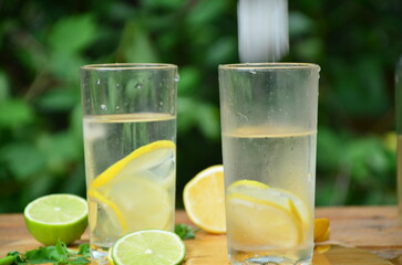 Fresh summer drink. Cold lemonade with mint lemon and lime on a nature outdoor background. Mojito summer refreshing cocktail with ice and mint