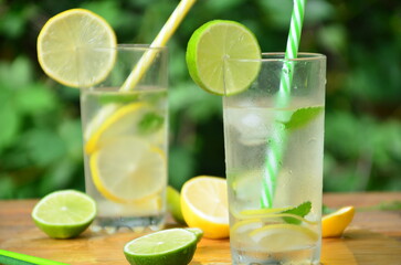 Fresh summer drink. Cold lemonade with mint lemon and lime on a nature outdoor background. Mojito summer refreshing cocktail with ice and mint
