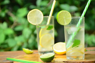 Fresh summer drink. Cold lemonade with mint lemon and lime on a nature outdoor background. Mojito summer refreshing cocktail with ice and mint