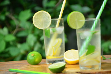 Fresh summer drink. Cold lemonade with mint lemon and lime on a nature outdoor background. Mojito summer refreshing cocktail with ice and mint