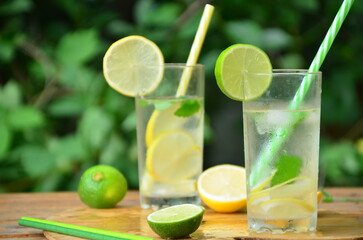 Fresh summer drink. Cold lemonade with mint lemon and lime on a nature outdoor background. Mojito summer refreshing cocktail with ice and mint