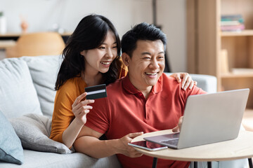 Cheerful chinese man and woman using laptop and credit card