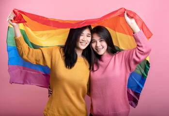 Two handsome gay girls stand with rainbow flags on pink backs in support of LGBT pride.