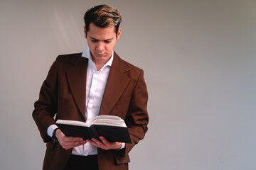 Caucasian blond man elegantly dressed in a suit, shirt and a watch reading a book on a white...