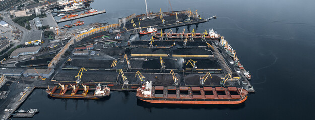 Loading coal anthracite mining in port on cargo tanker ship with crane bucket of train. Aerial top view - obrazy, fototapety, plakaty