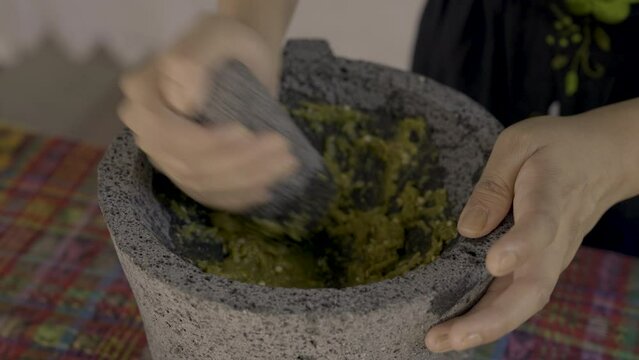 Indigenous woman's hands making green salsa on a molcajete. 