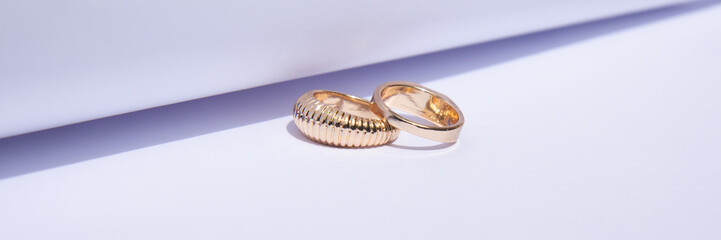 Two gold wedding rings on a white background with contrasting shadows. Banner