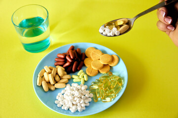 A handful of pills, capsules and multi-colored tablets on a plate next to cutlery. Taking medication. Pills instead of food. The concept of vitamins instead of food