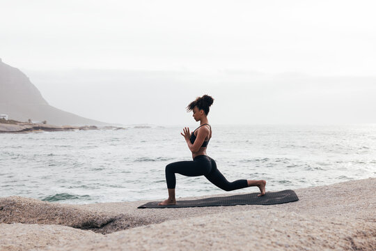 Woman in fitness wear practicing yoga on a mat at seashore - Powered by Adobe