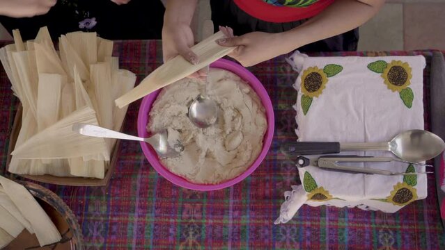 Indigenous women's hands putting masa in a corn husk to make tamales. 
