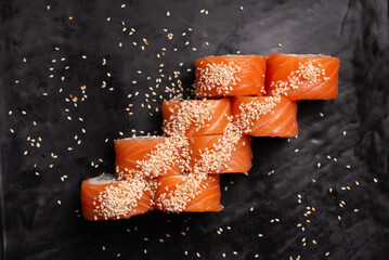 Philadelphia Maki raw red Salmon Roll set covered with sesame seeds on black surface flat lay