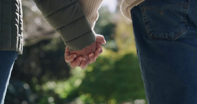 Loving, affectionate and a couple holding hands while enjoying a romantic walk in a park on a sunny day outside. Closeup of a husband and wife in a happy marriage walking while relaxing together