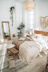 Cozy rustic bedroom with boho ethnic decor. Enter apartment with sun rays from large windows and wooden furniture. Console table, full-length mirror and handmade textiles. Plants in the interior © Sheremetio