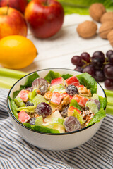 Waldorf salad of apples, celery stalks, walnuts, grapes, lettuce in a white salad bowl with ingredients on an old rustic white wooden table. Selected focus. - 524124977