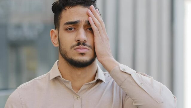 Close up portrait upset looser sad frustrated disappointed failure Arabian Hispanic Indian businessman face palm reaction stress with problem bearded man lost trouble unpleasant worry outdoors in city