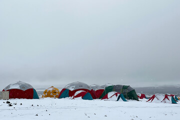 Snow covered campsite and tents of a scientific research expedition on a pumice stone field in...