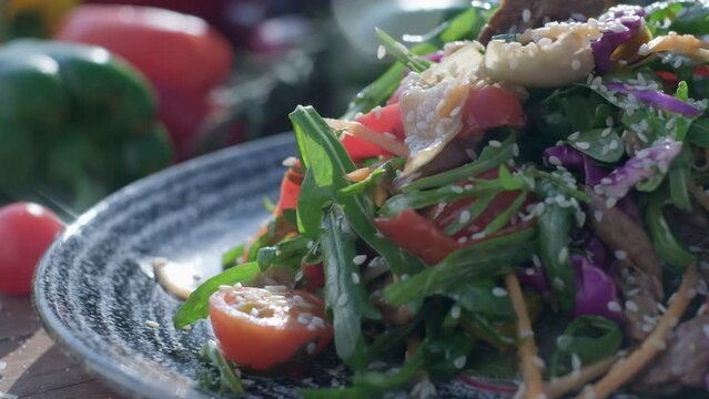 Close-up of fresh salad made of red cabbige, tomatoes, onions, basil, arugula and pieces of fried meat
