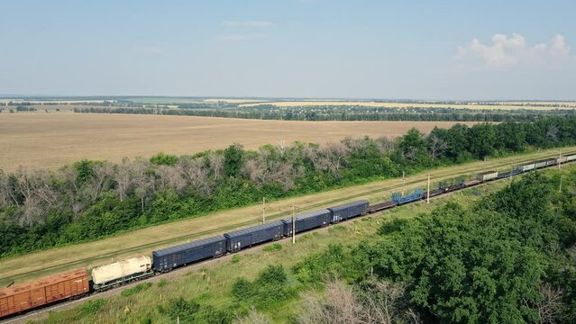 Long freight train rolling by a rural area, aerial view