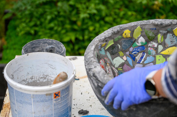 People decorate earthenware with mosaic techniques in the master class or in the fresh air in the workshop. Homemade mosaic flower pot with porcelain pieces.