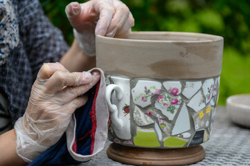 People decorate earthenware with mosaic techniques in the master class or in the fresh air in the workshop. Homemade mosaic flower pot with porcelain pieces.