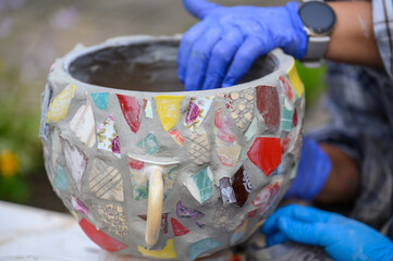 People decorate earthenware with mosaic techniques in the master class or in the fresh air in the workshop. Homemade mosaic flower pot with porcelain pieces.