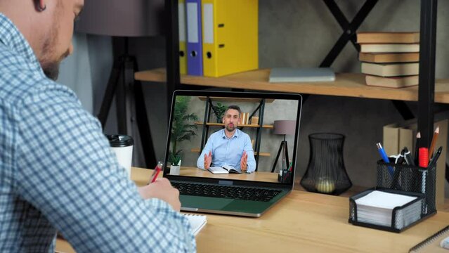 Online business meeting. Businessman at home office listen top manager remote video call webcam chat laptop, writes in notebook. Man employee in computer screen tells report on company performance