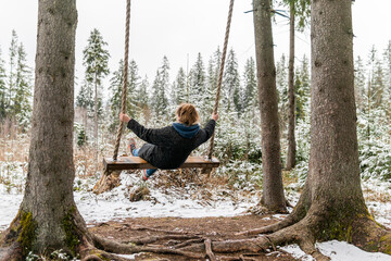 Poland, Rabka-Zdroj  – April 10, 2022: A pregnant woman is swinging outdoors in winter with amazing view on the forest - obrazy, fototapety, plakaty