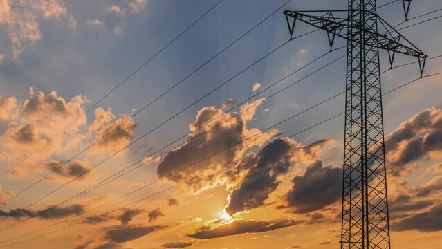Time lapse of single power transmission pylon in front of dramatic sunset with menacing clouds floating across the sky.
