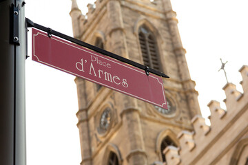 Selective focus low angle view of Place d’Armes red street sign with patrimonial 1829 Notre-Dame...